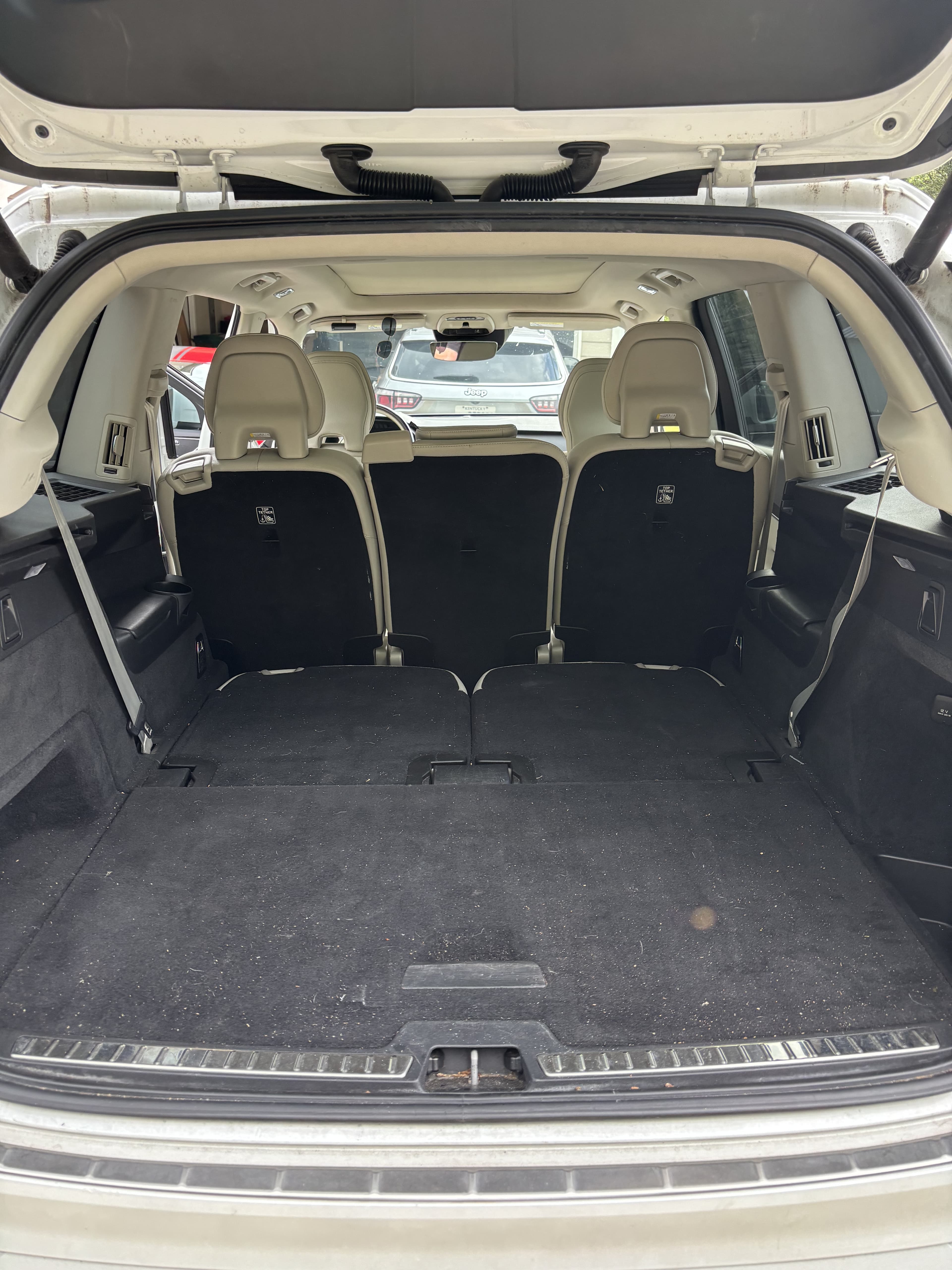 Open rear hatch of a white SUV revealing a spacious black carpeted cargo area.