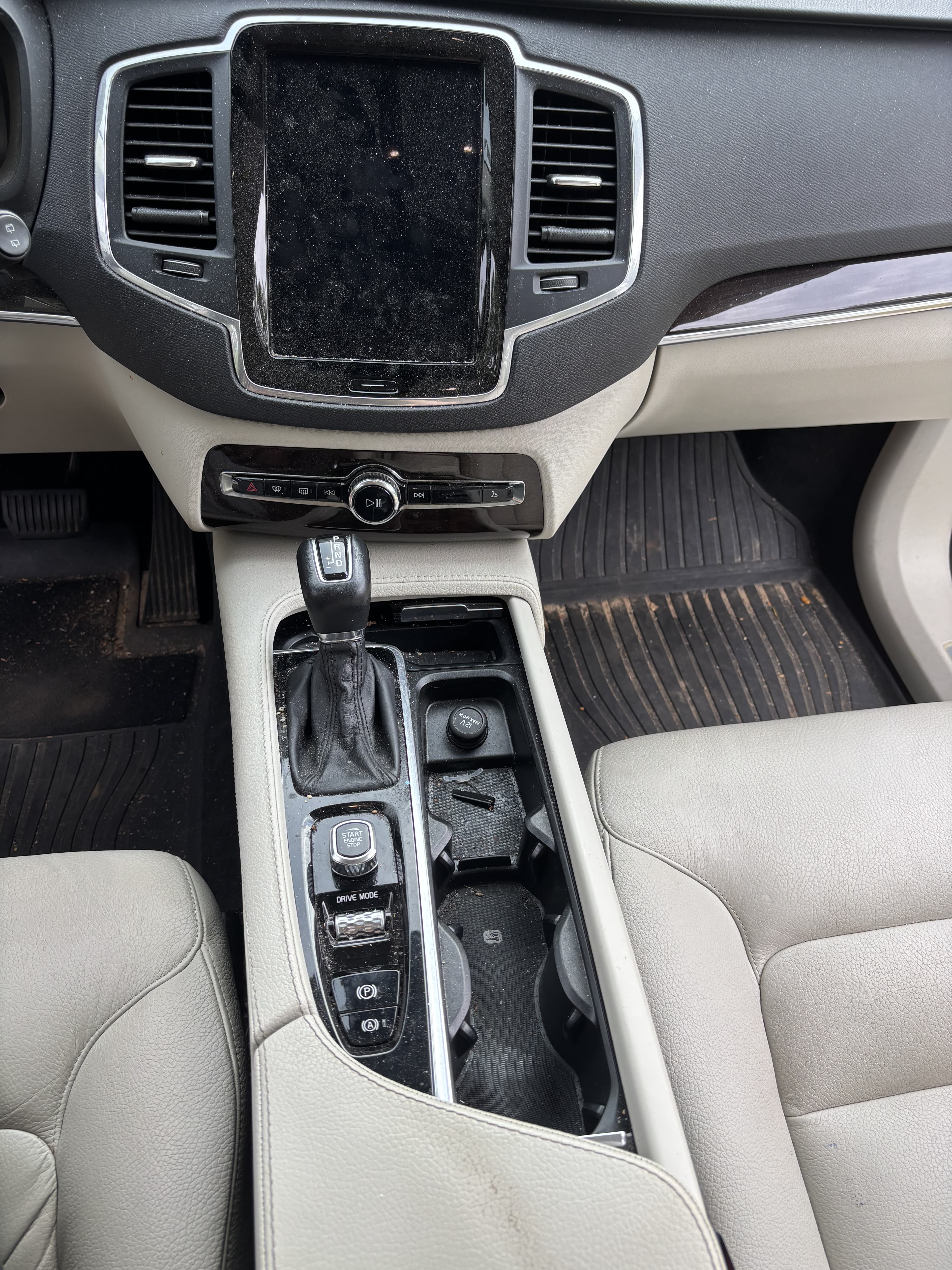 Interior of a car featuring a large vertical touchscreen, gear shifter, and light leather seats.