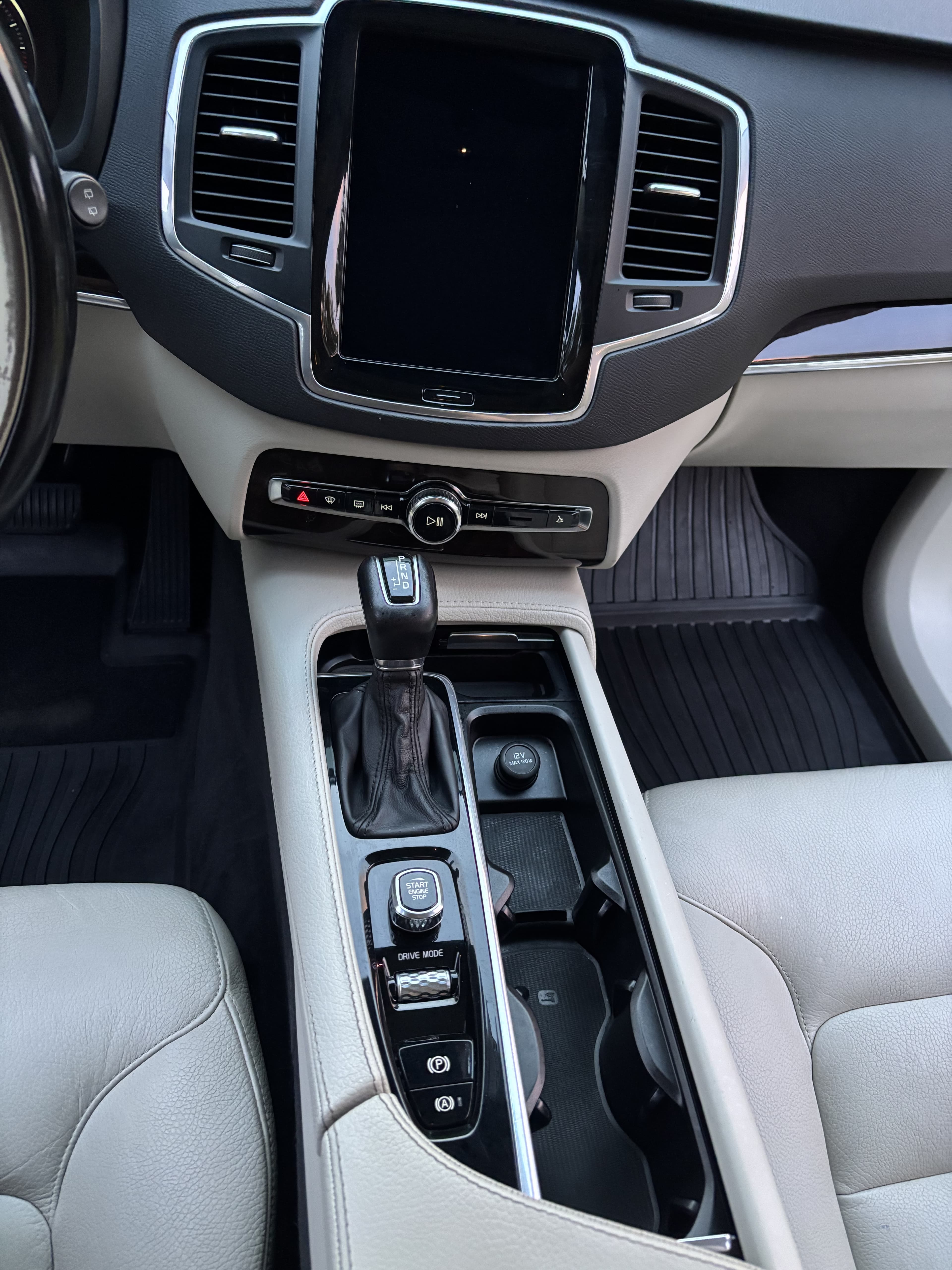 Modern car interior featuring a large vertical touchscreen, gear shifter, and light gray leather upholstery.