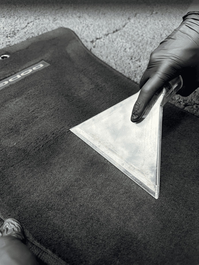Gloved hand using a clear vacuum extractor to deep clean a black Dodge floor mat.